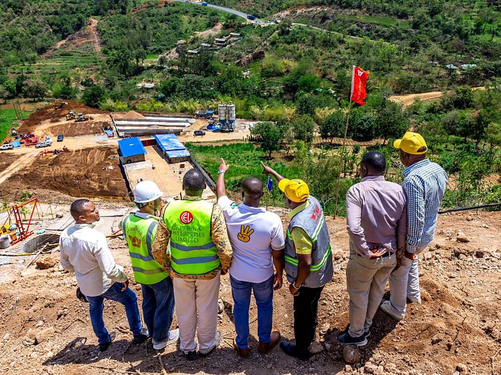 People in hard hats and reflective vests look over the Nithi bridge construction site in a green valley
