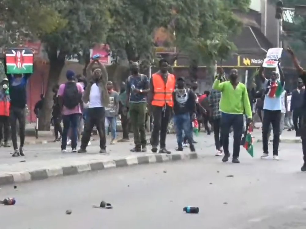 Protesters, some holding Kenyan flags and placards, standing on a road in central Nairobi