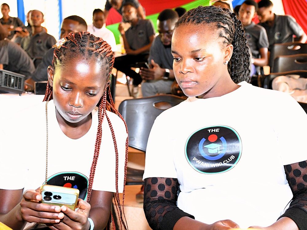 Two students at Pwani University looking at a phone during an event